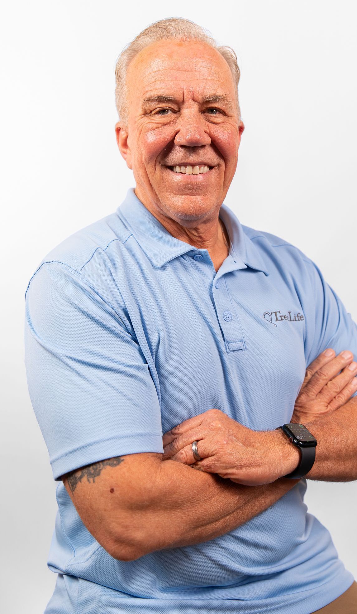 A TreeLife professional in a blue shirt is standing with his arms crossed and smiling.