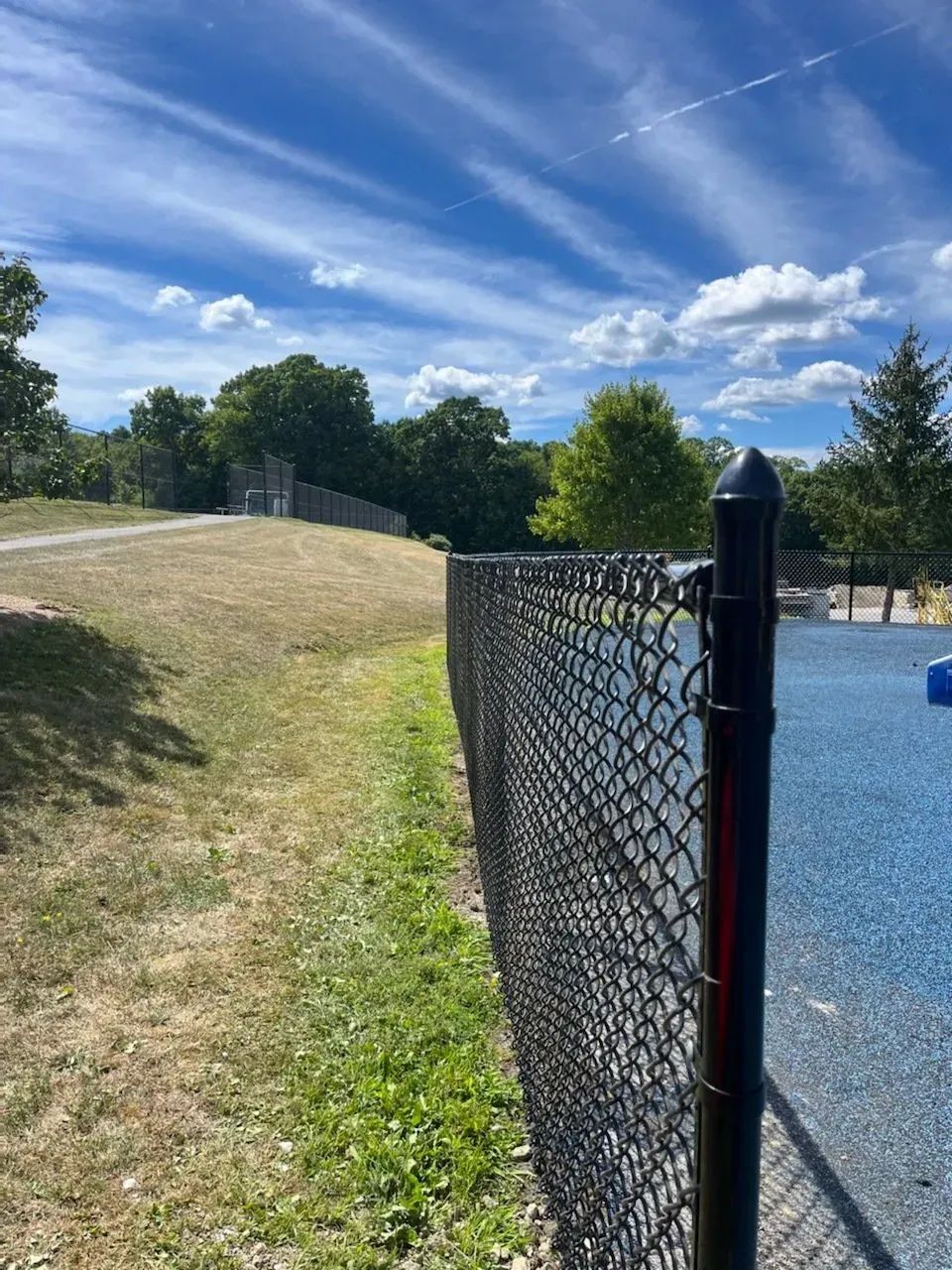 A chain link fence surrounds a playground in a park.