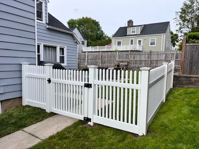 A white picket fence with a gate in front of a house.