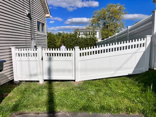 White vinyl fence and gate along a grassy yard beside a house under a blue sky