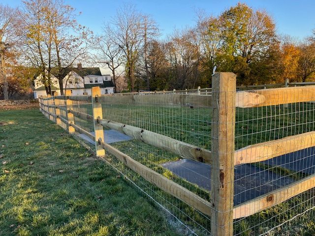 A wooden fence surrounds a grassy field with a house in the background.