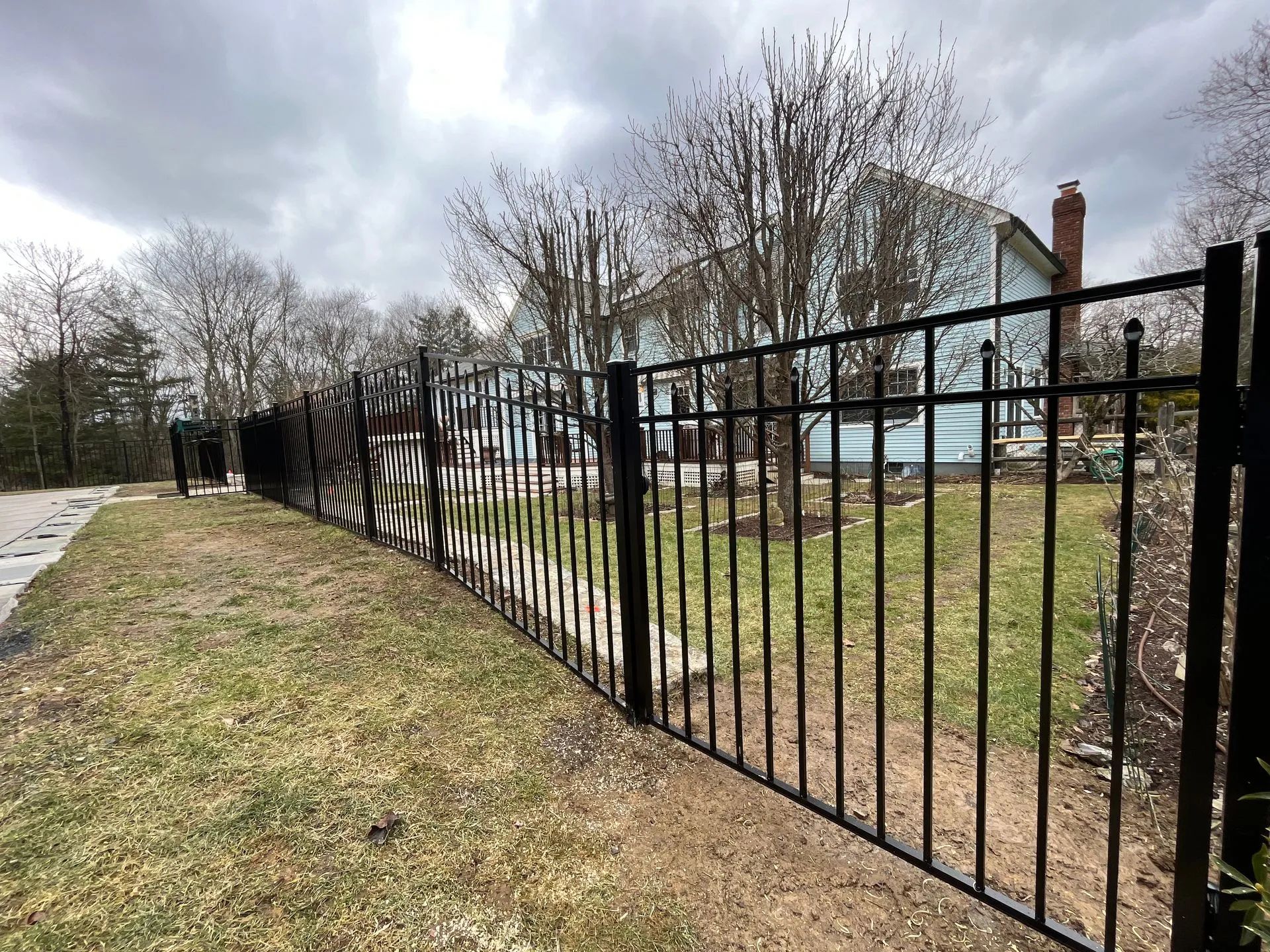 Black metal fence along a grassy path beside a road under cloudy skies