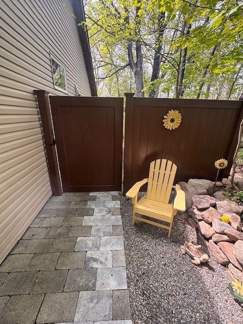 Outdoor patio with tan chair, stone walkway, brown fence, and rock garden beside a house