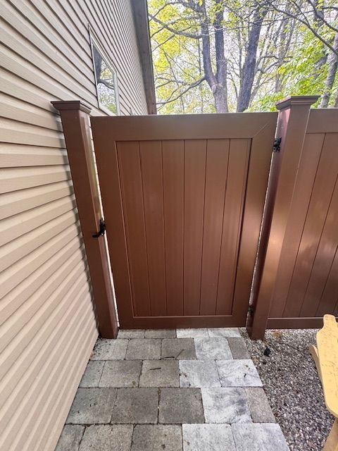 Narrow backyard gate between beige siding and wooden fence, with gray paver path leading to it.