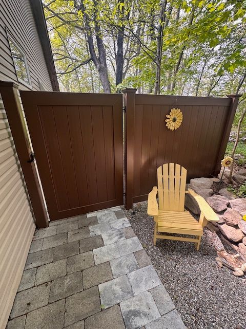 Backyard patio with brown privacy gate, stone pavers, yellow chair, and decorative wall flower.