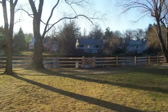 A wooden fence surrounds a grassy field with trees in the background.