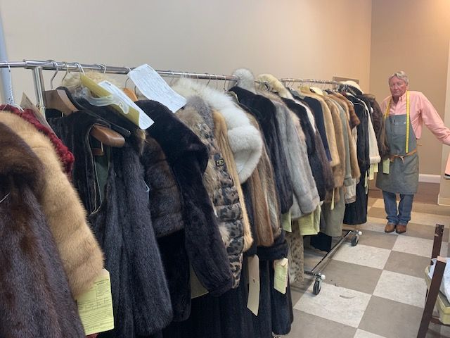 A woman is standing in front of a rack of fur coats