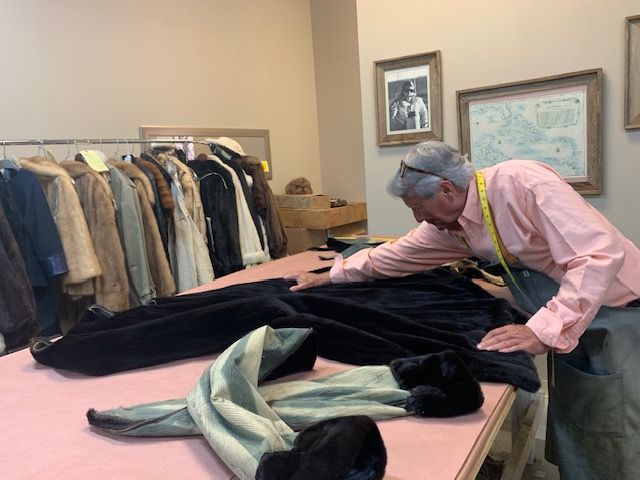 A man in a pink shirt is working on a fur coat