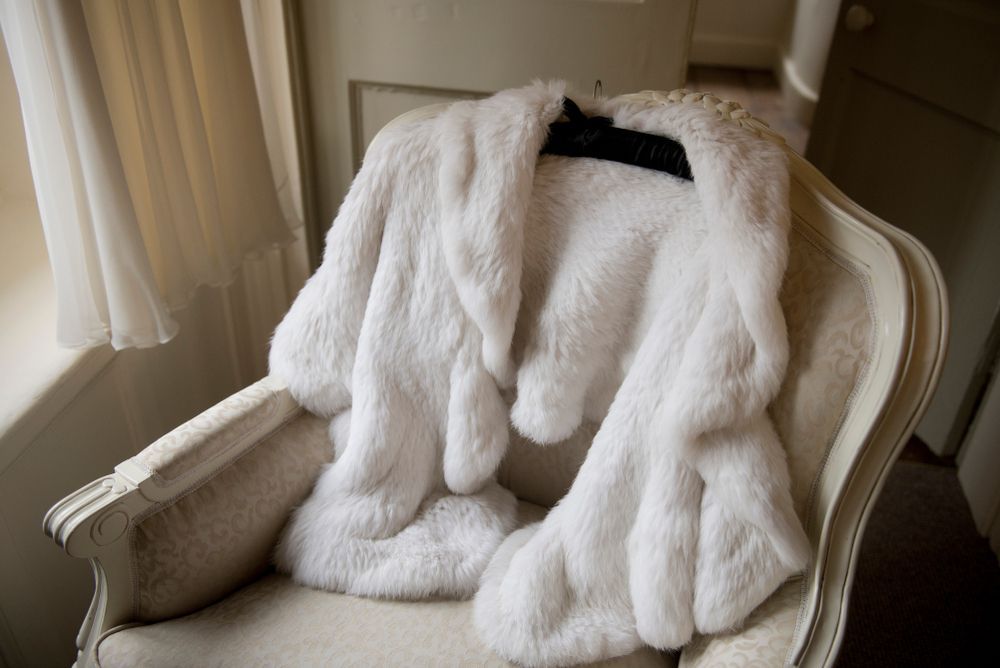 A white fur coat is sitting on a chair in front of a window.