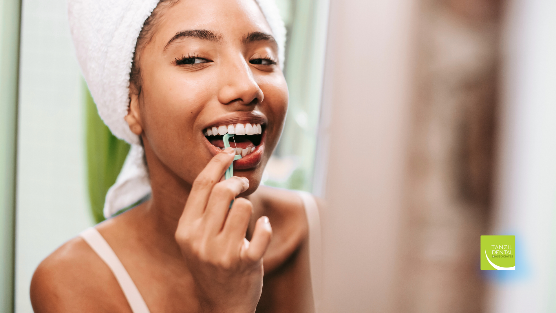 A woman with a towel wrapped around her head is brushing her teeth in front of a mirror.