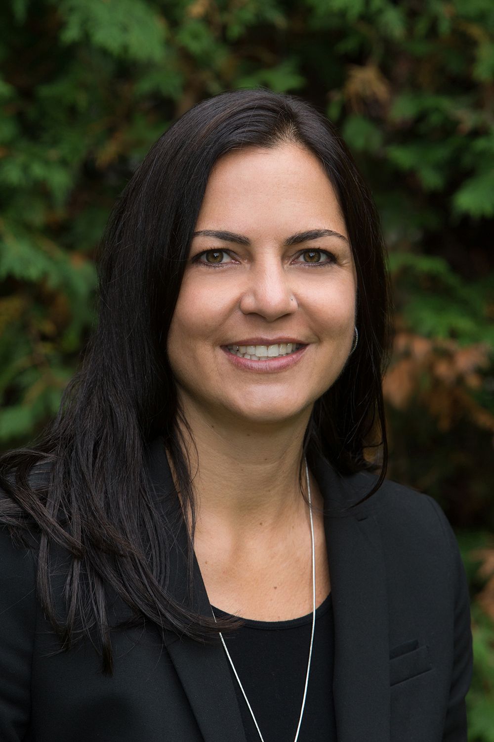 A woman in a black jacket and necklace is smiling for the camera.