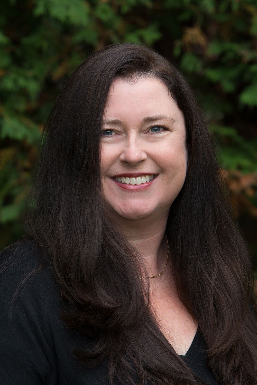 A woman with long brown hair is smiling and wearing a black shirt.