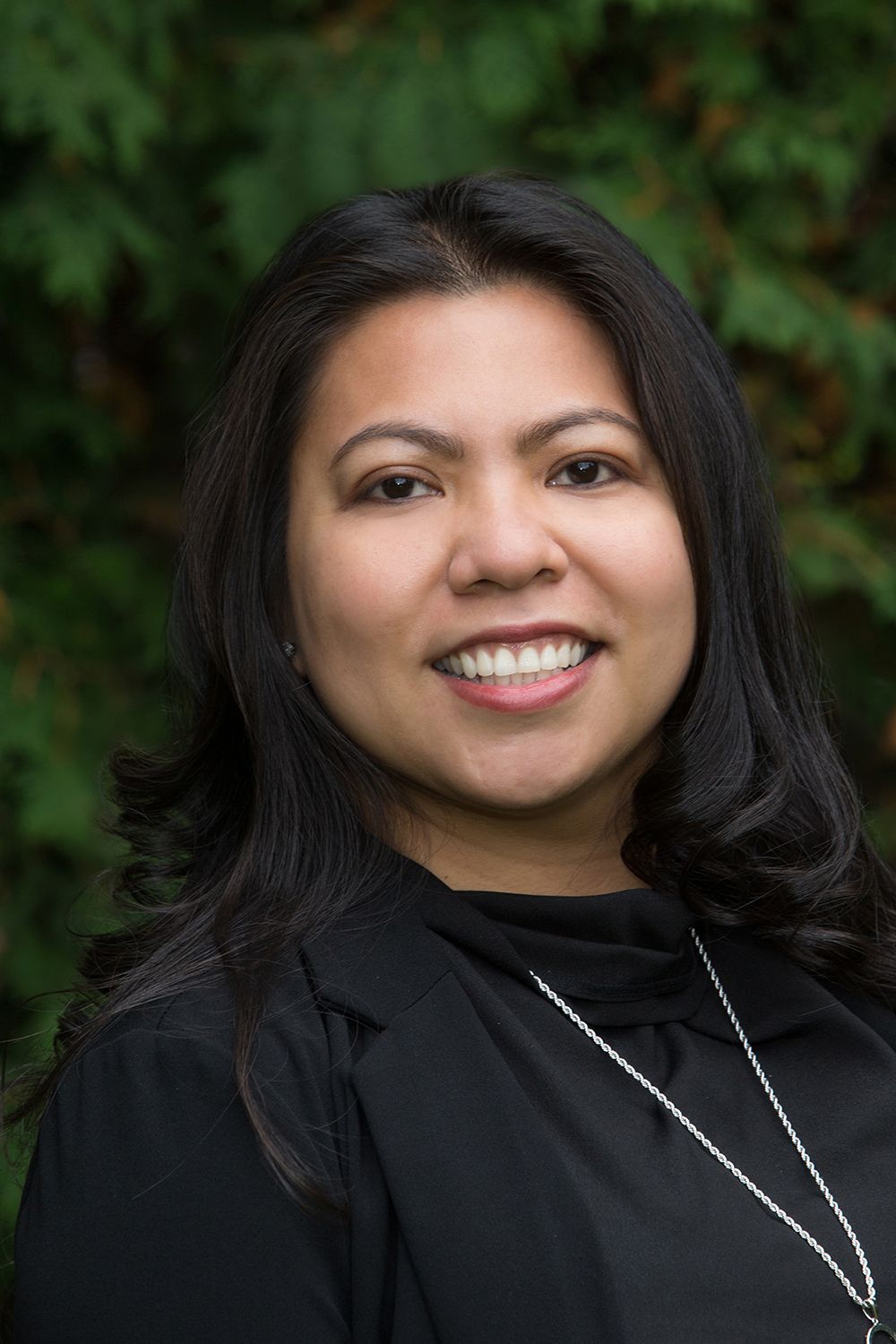 A woman in a black shirt and necklace is smiling for the camera.