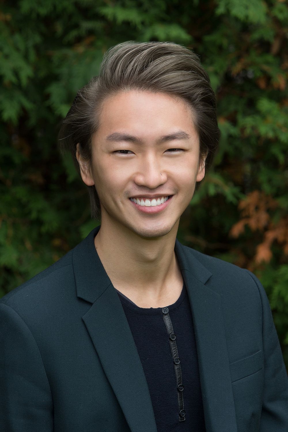 A young man in a suit and sweater is smiling for the camera.