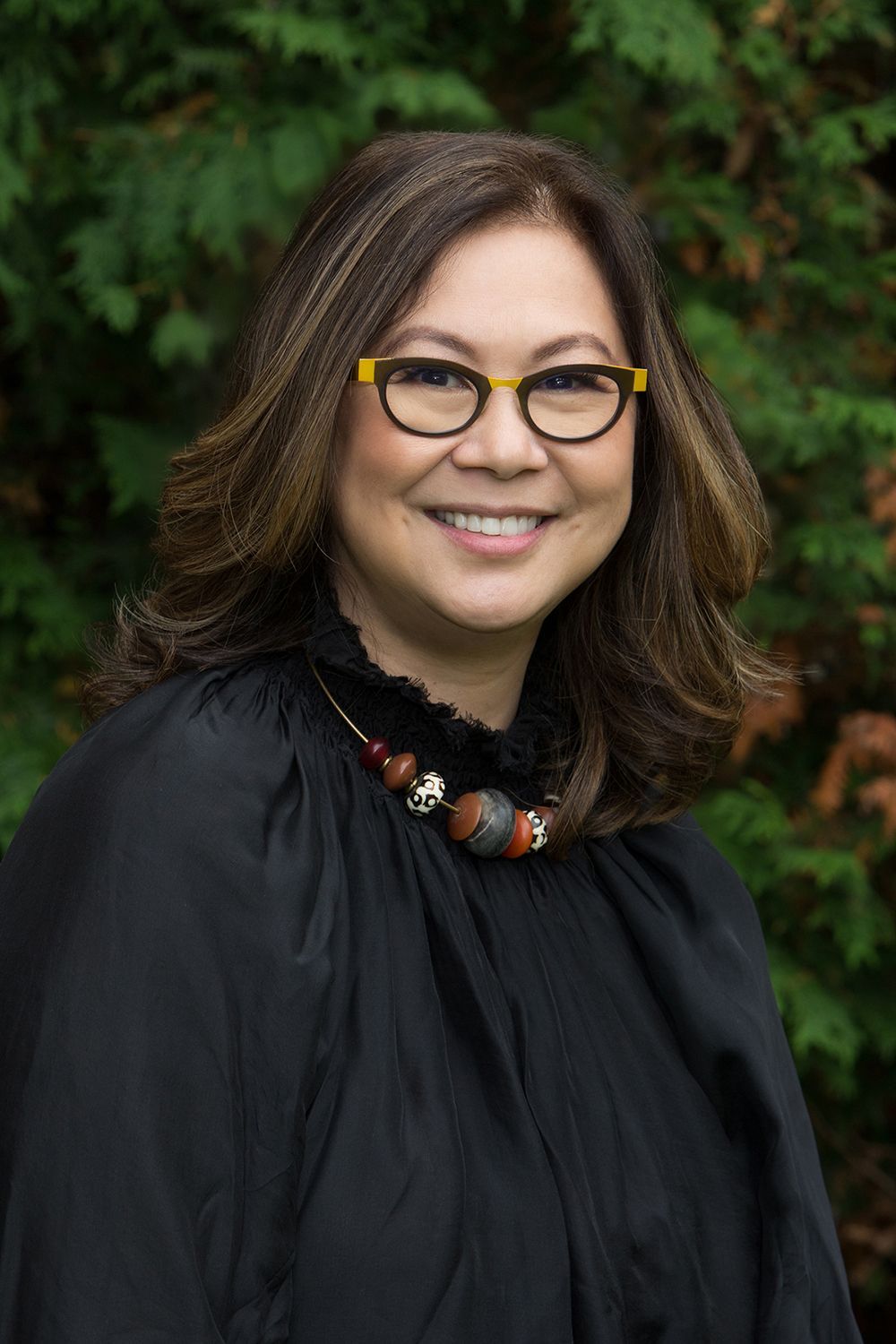 A woman wearing glasses and a necklace is smiling for the camera.