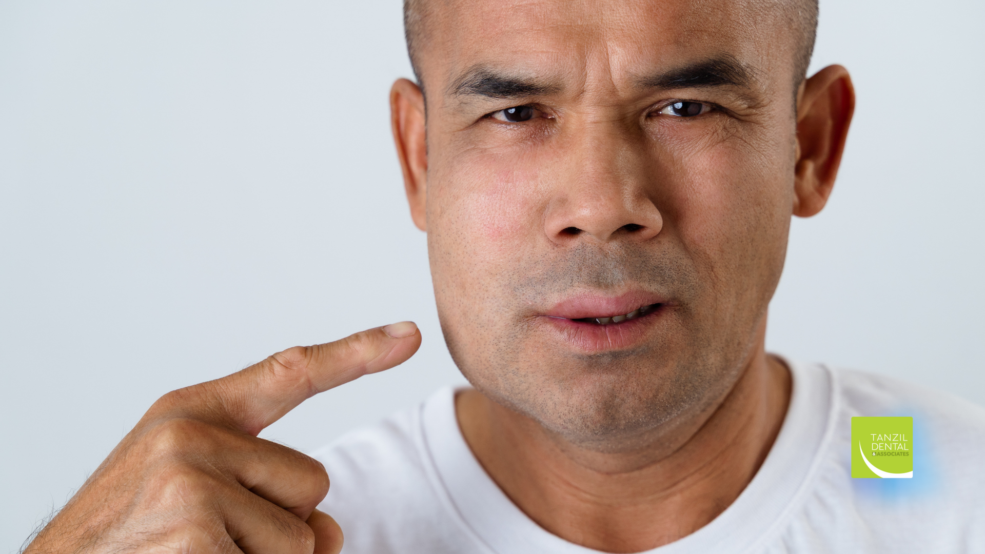 A man in a white shirt is pointing at his face.