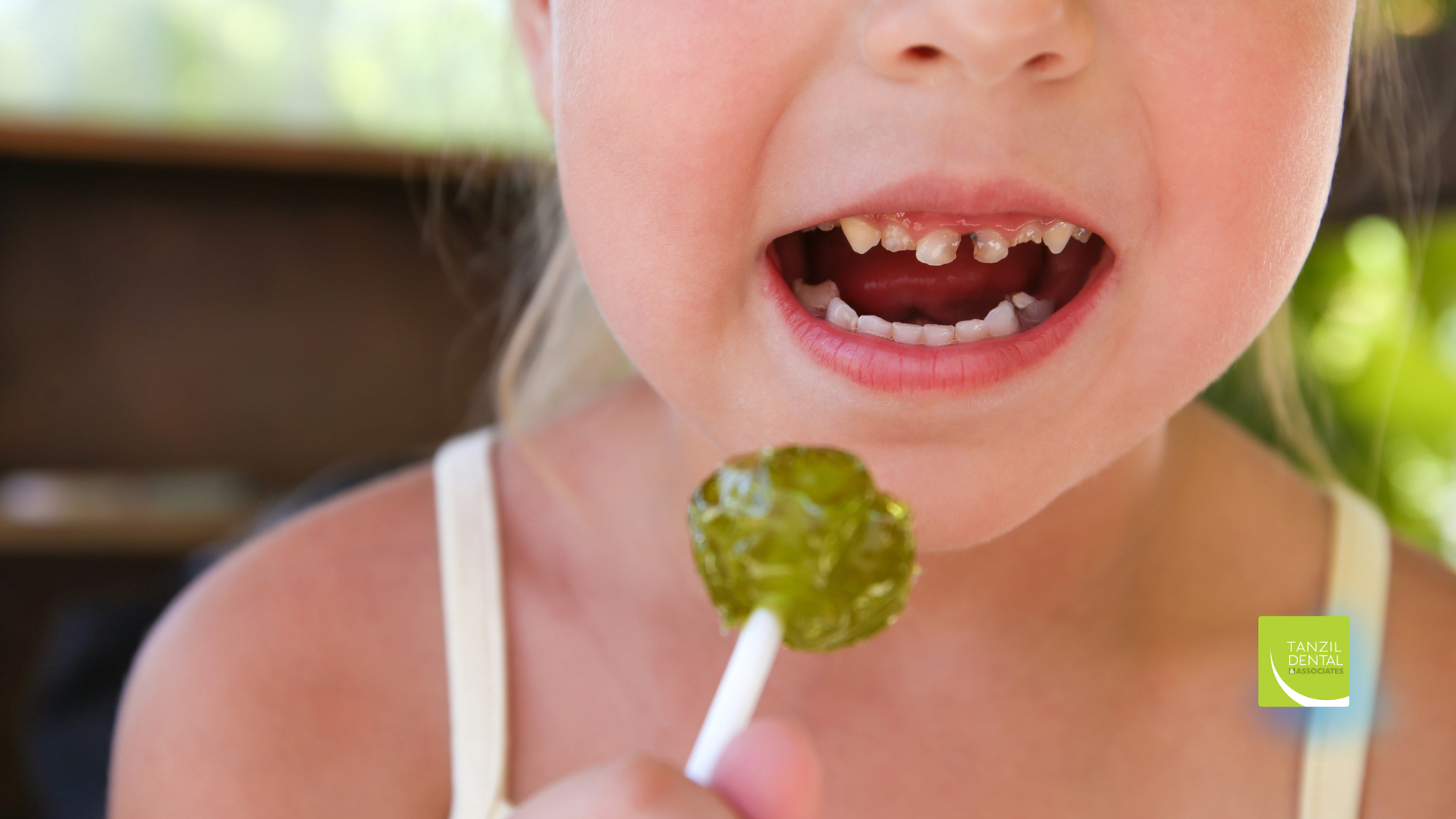 Young child with missing front teeth holding a green lollipop.