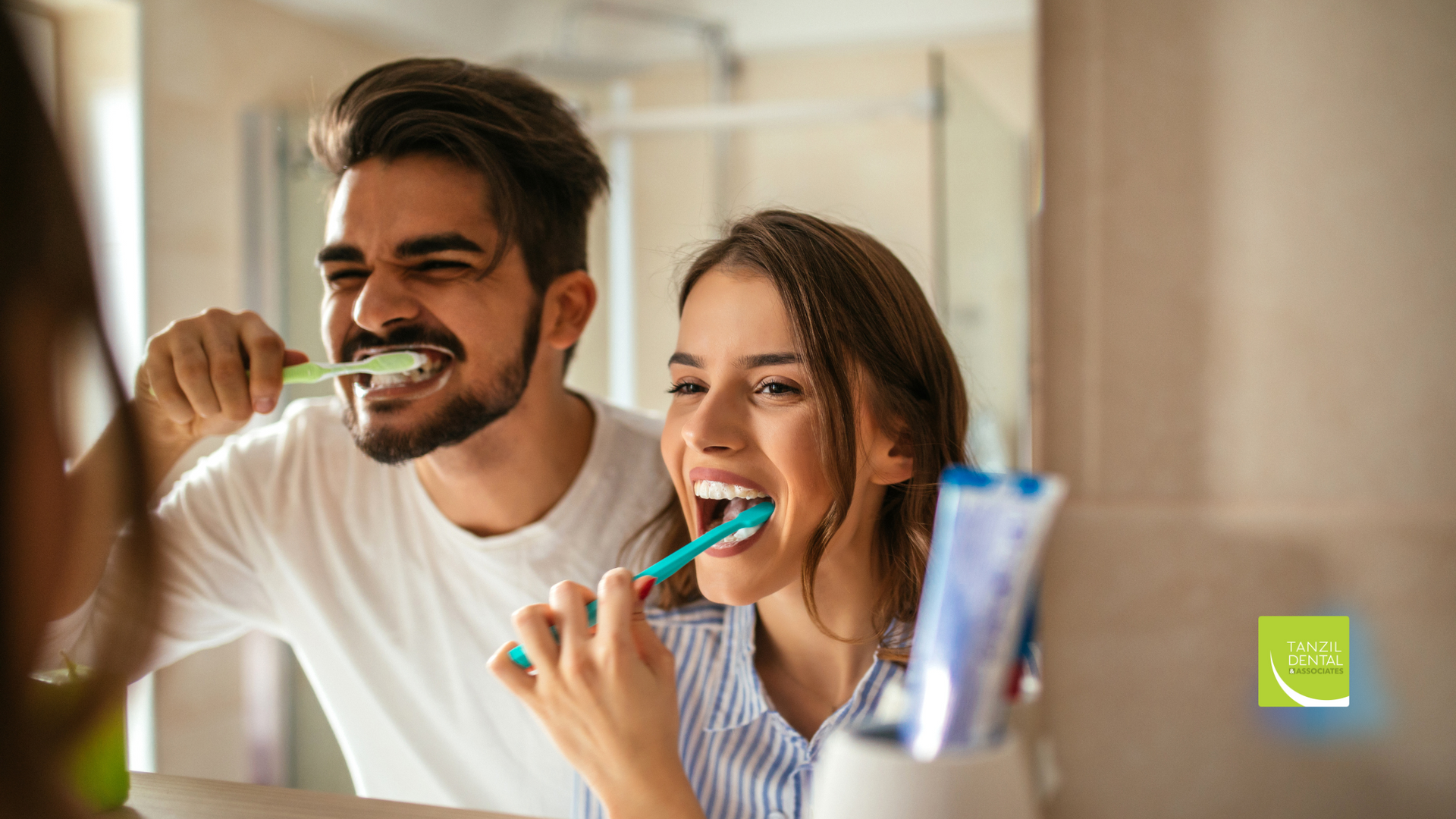 A man and a woman are brushing their teeth together in front of a mirror.