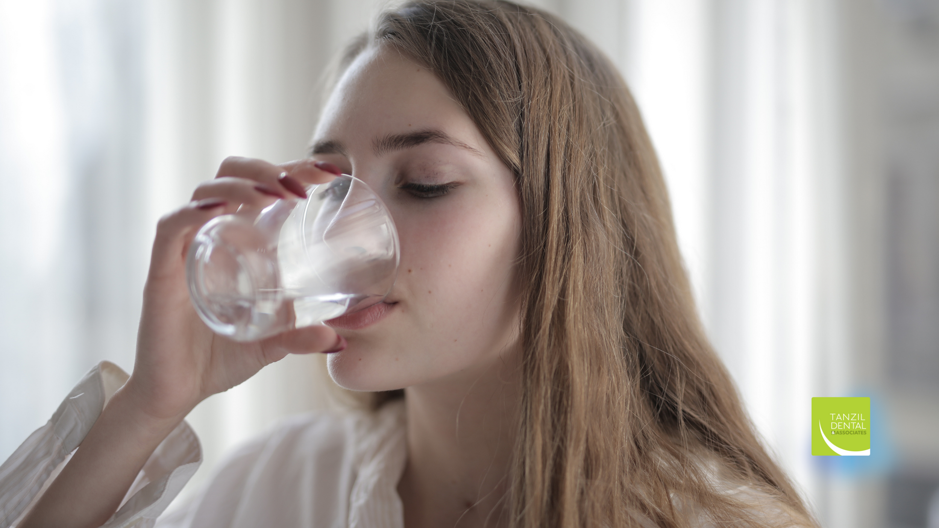 A woman is drinking water from a glass.