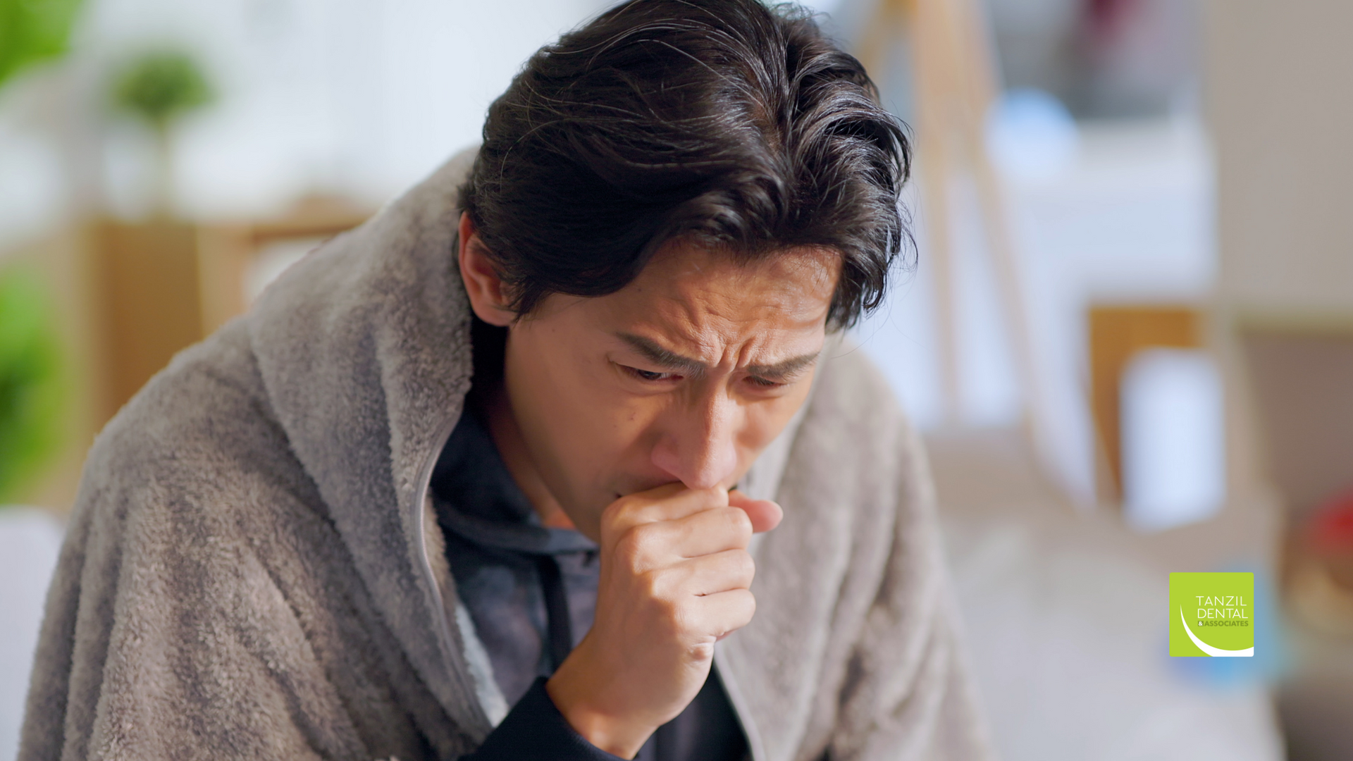 A man wrapped in a blanket is coughing while sitting on a couch.