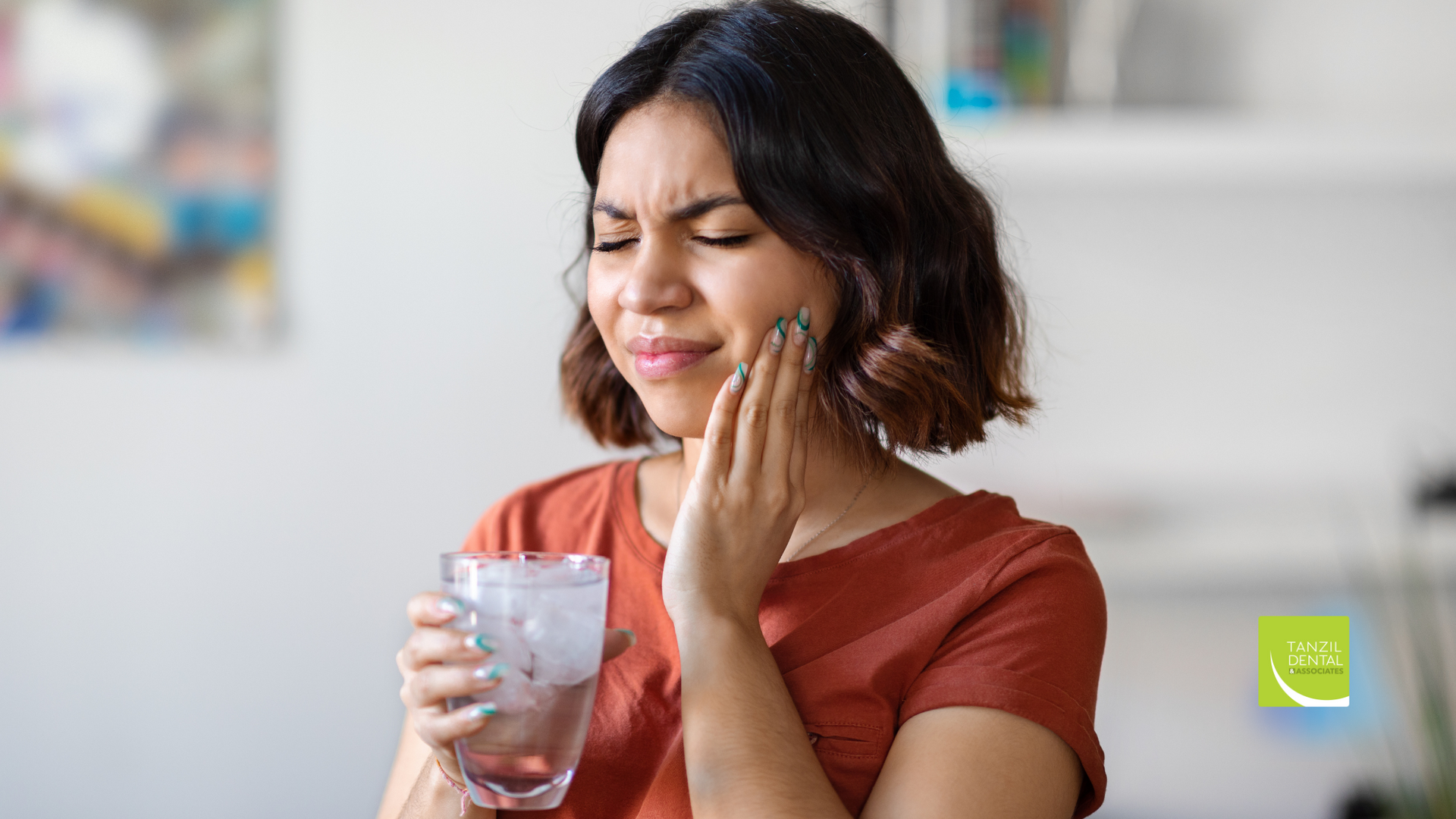 A woman is holding a glass of water and having a toothache.