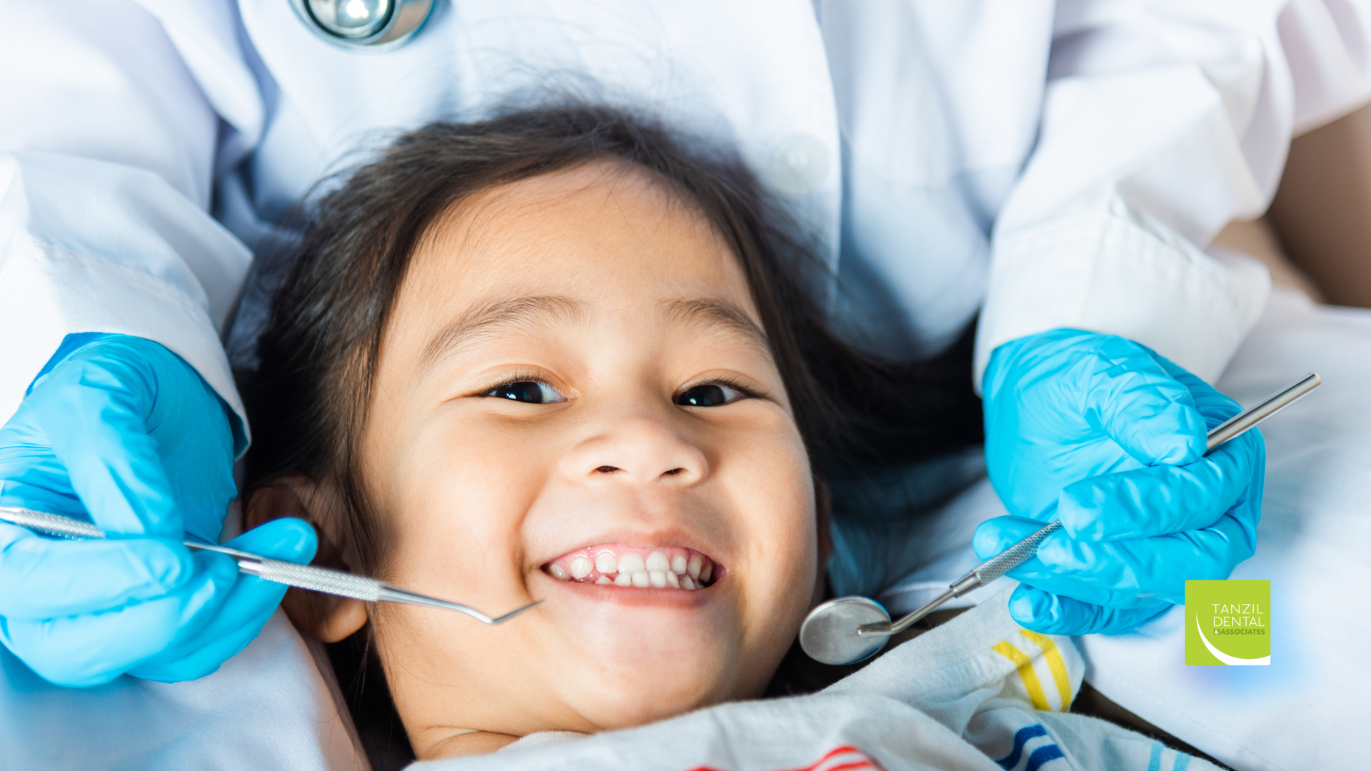 Child smiling at dentist during a check-up. Dentist in blue gloves holds tools.