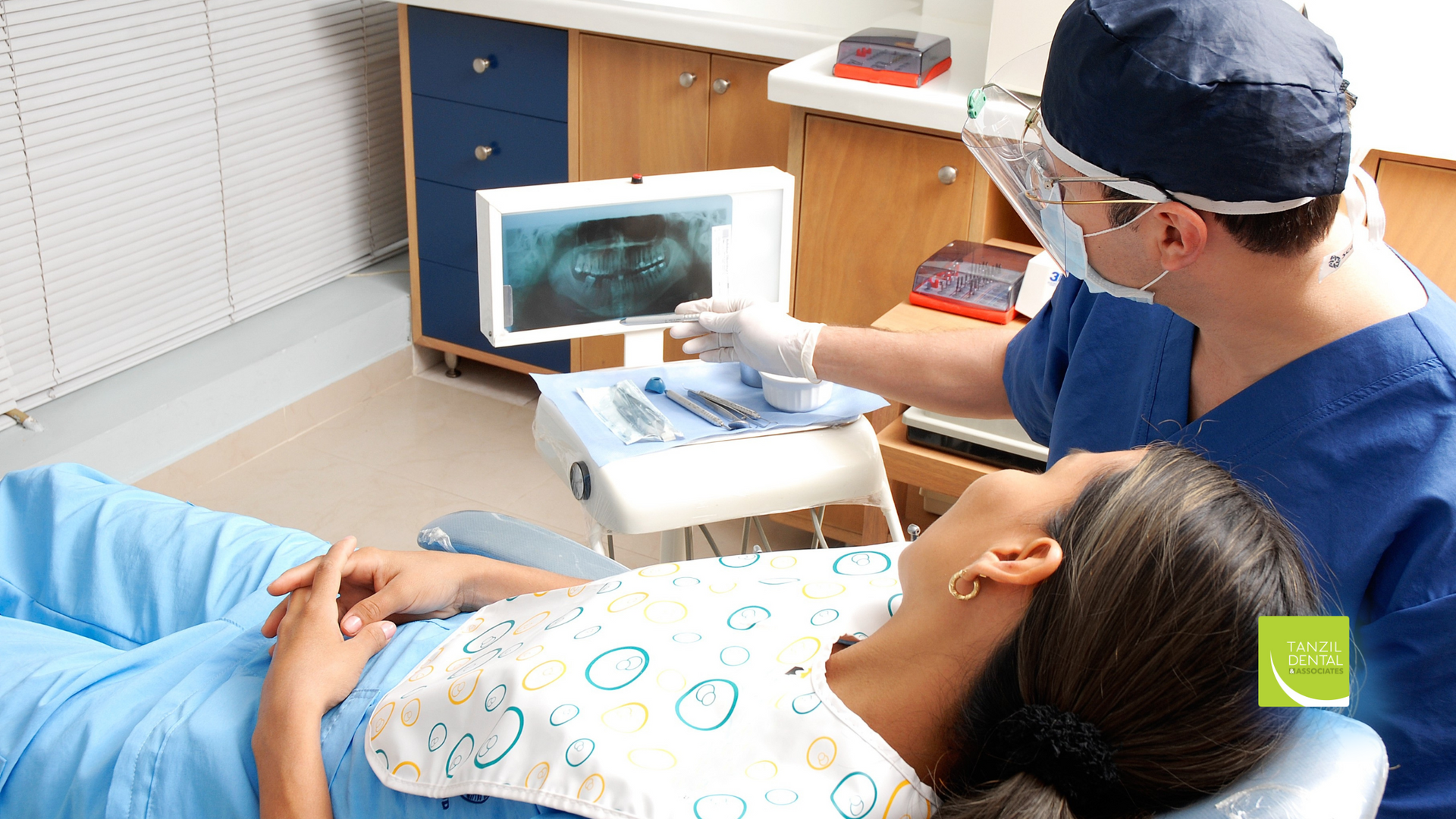 Dentist examining an x-ray with a patient in a dental chair in a clinic.