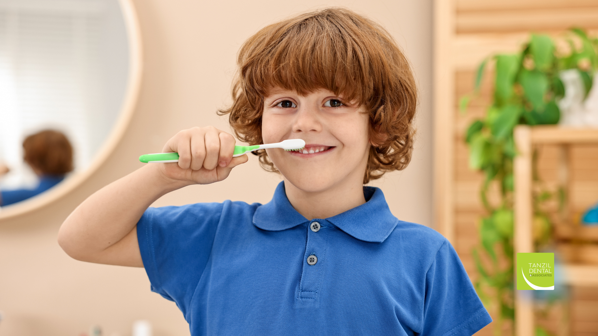 Boy in blue shirt brushing teeth in front of a mirror, smiling.