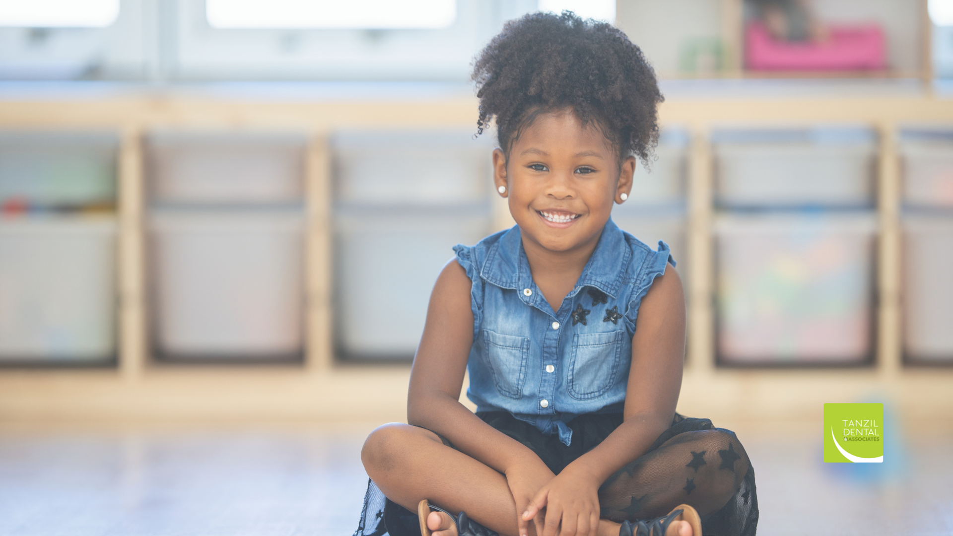 Smiling child in denim top and black skirt, sitting cross-legged.