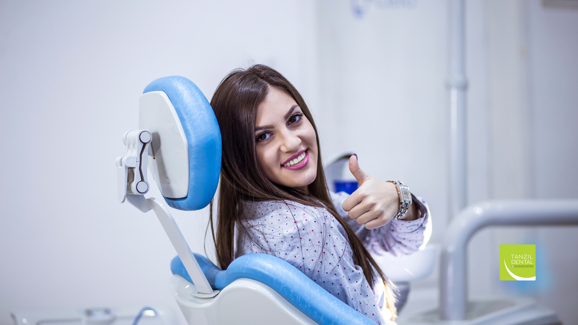 A woman is sitting in a dental chair and giving a thumbs up.