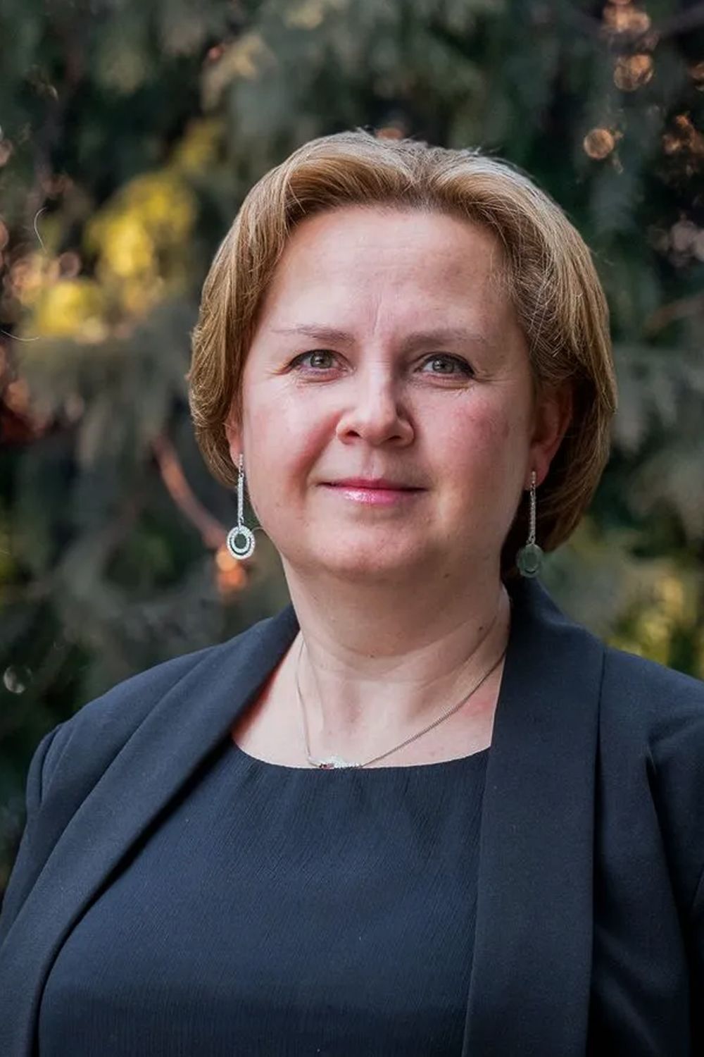 A woman in a black suit is standing in front of a tree.