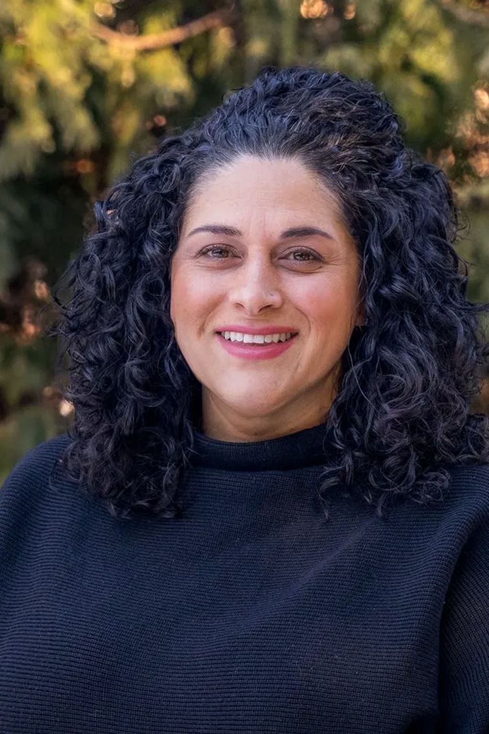 A woman in a black sweater is standing in front of a tree.