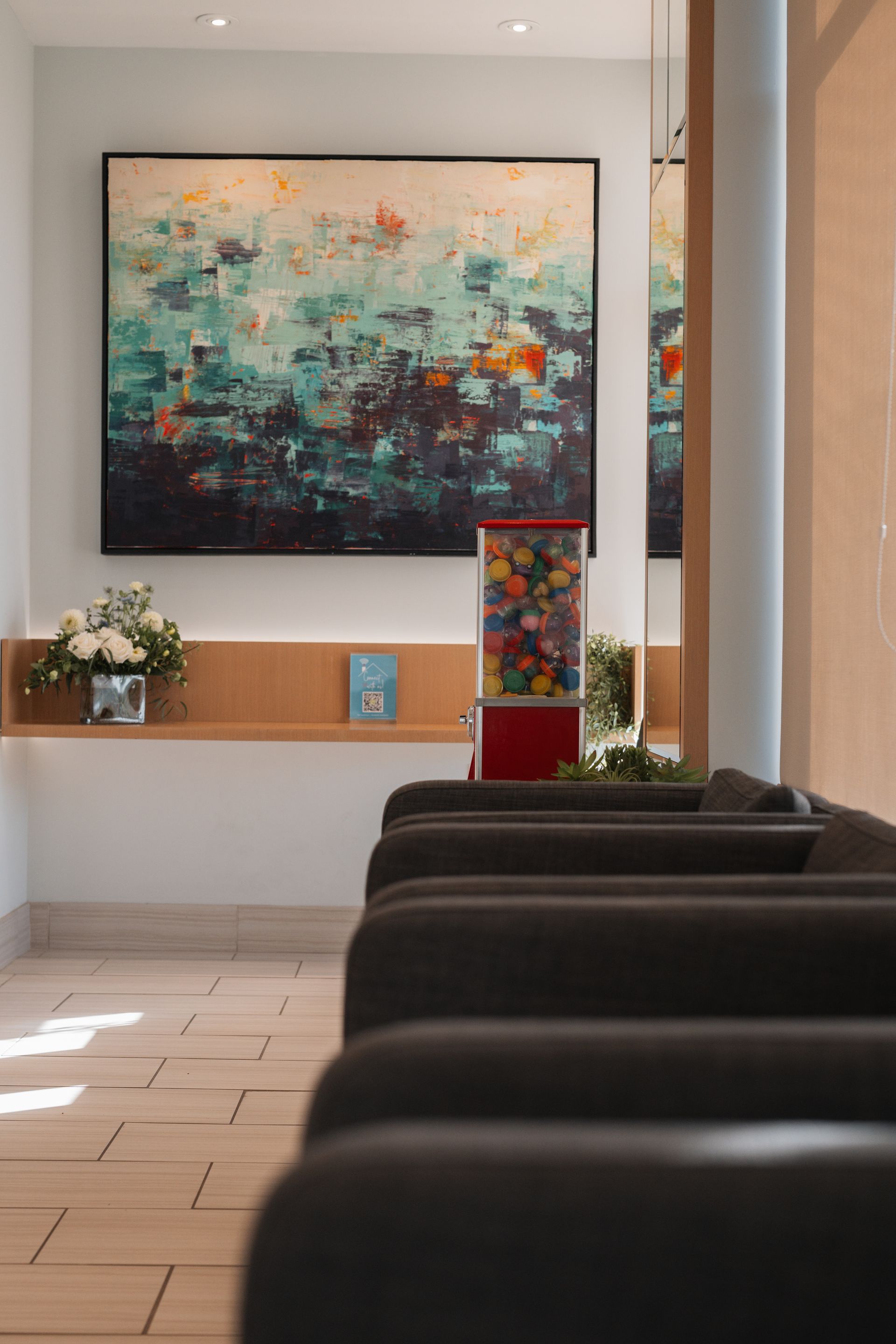A waiting room with a gumball machine and a painting on the wall.