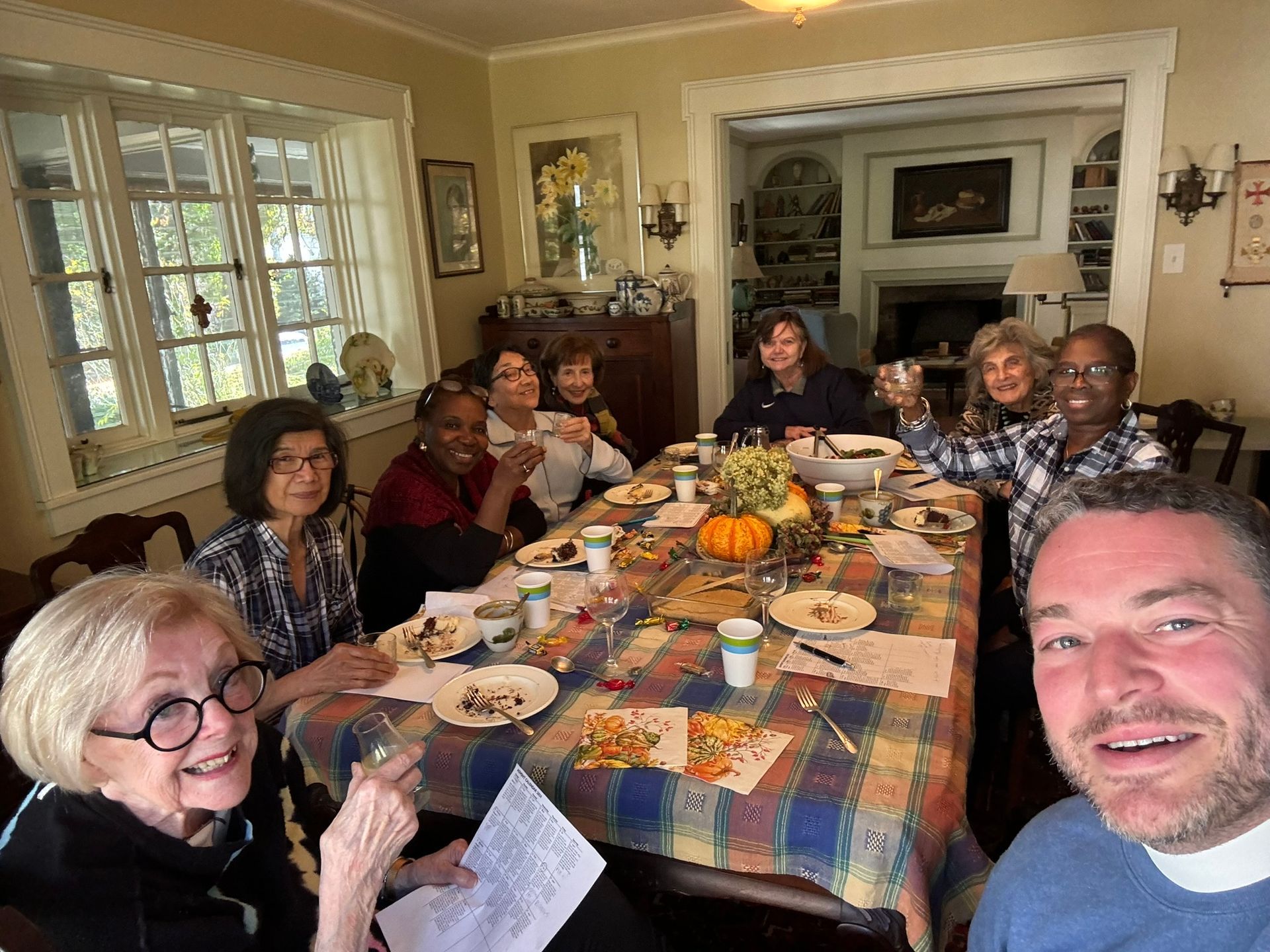 A group of people sitting around a table covered in a plaid tablecloth for a meal in a brightly lit dining room.