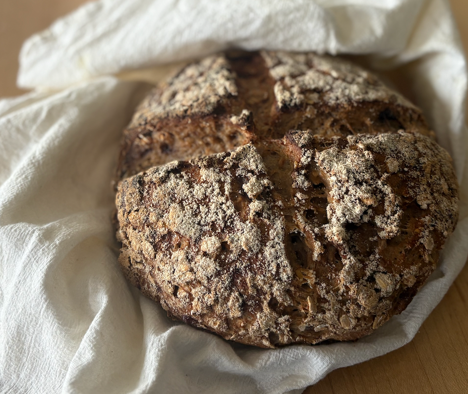 A crusty, seeded loaf of bread with a cross-shaped score on top, resting on a rumpled white cloth.