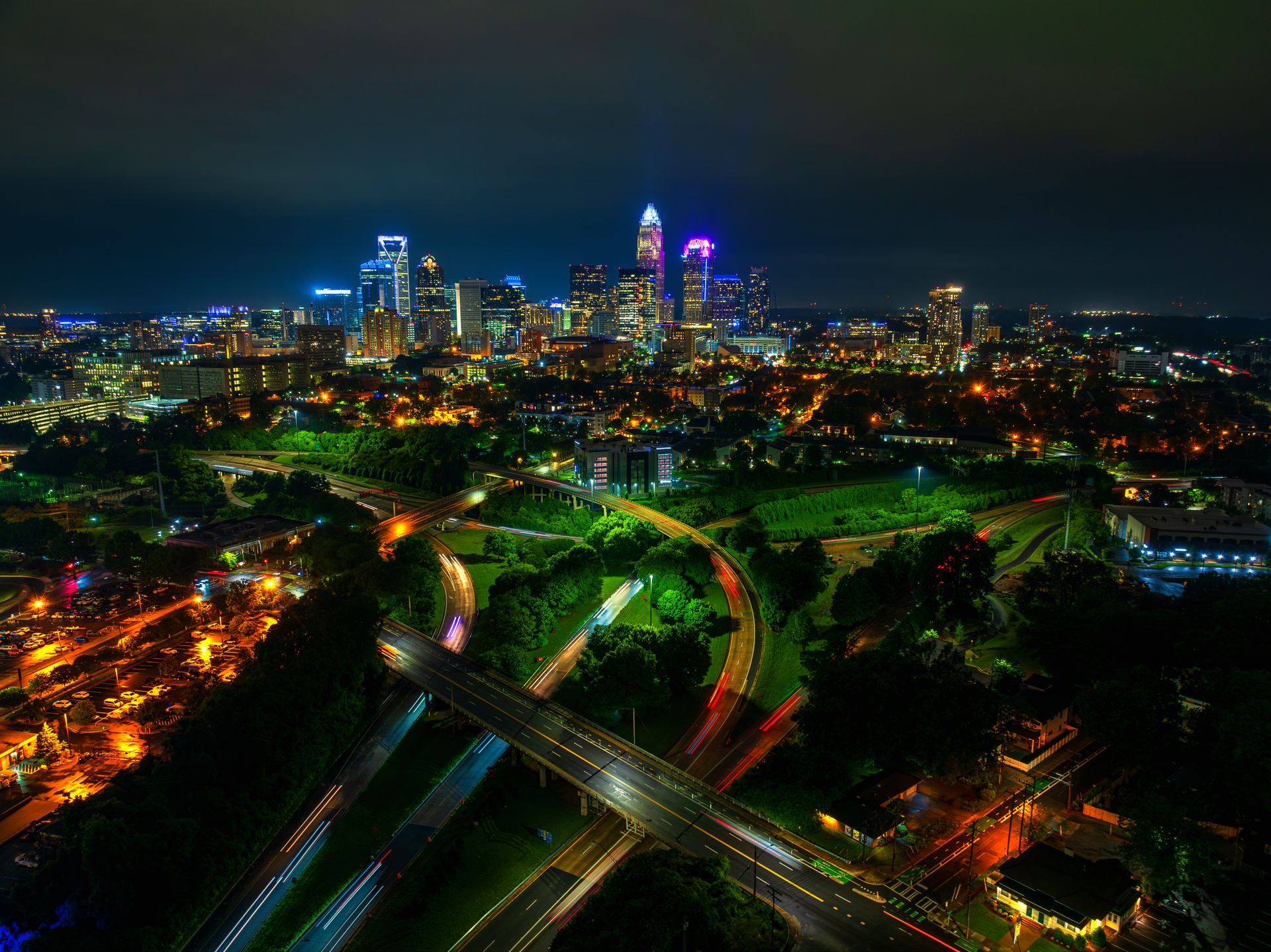 Nighttime aerial view of Charlotte, North Carolina's illuminated skyline and city lights, with highways below.