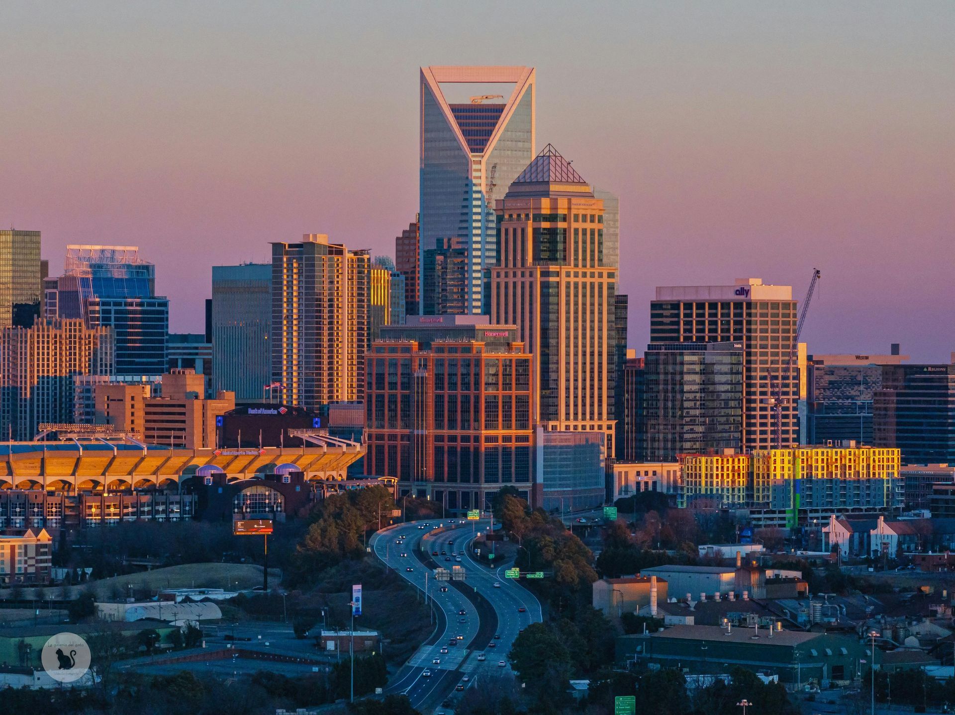 Charlotte, North Carolina skyline at sunset, featuring tall buildings and a highway with traffic.