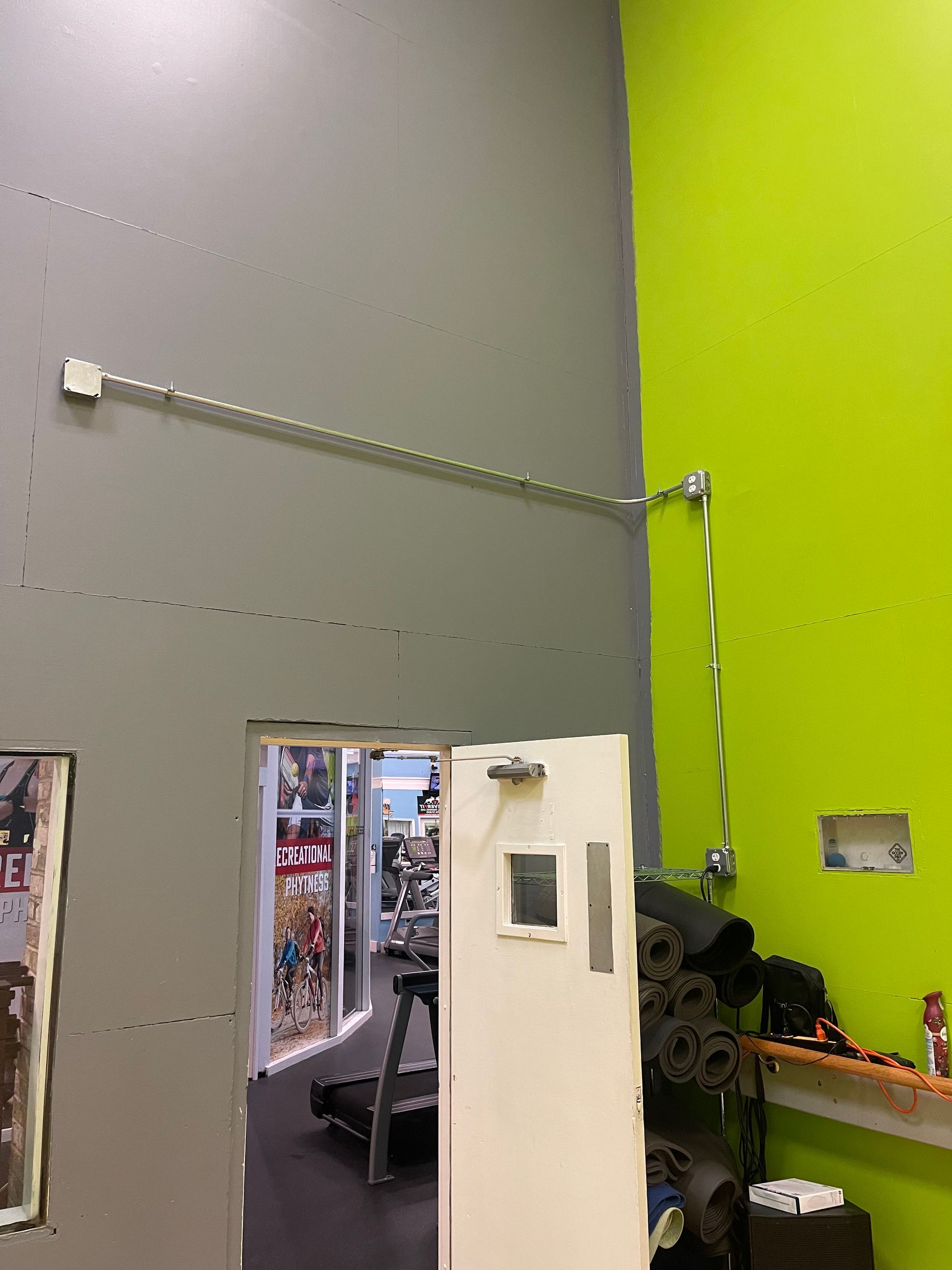 Conduit-mounted commercial electrical installation on painted gym wall