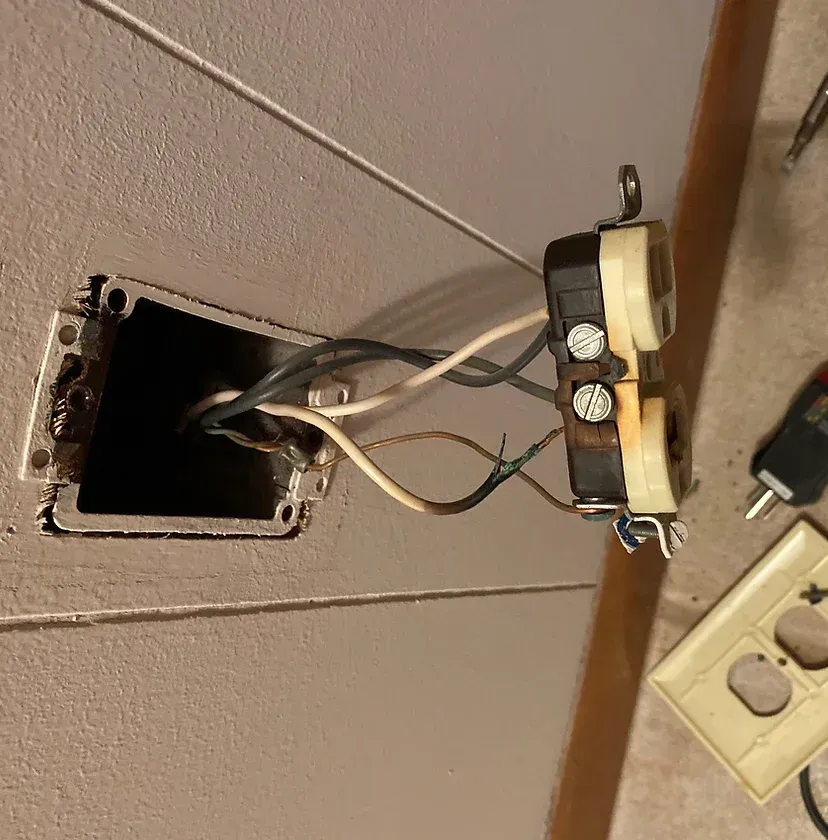Damaged wall outlet with exposed wiring during residential electrical repair service