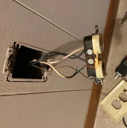Damaged wall outlet with exposed wiring during residential electrical repair service
