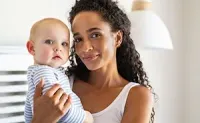 Woman holding a baby in a bright indoor setting, both looking at the camera.