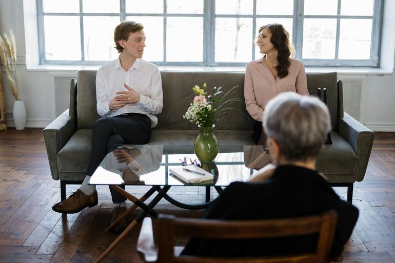 Two people seated on sofas in a bright 상담 room, facing a listener in the foreground.