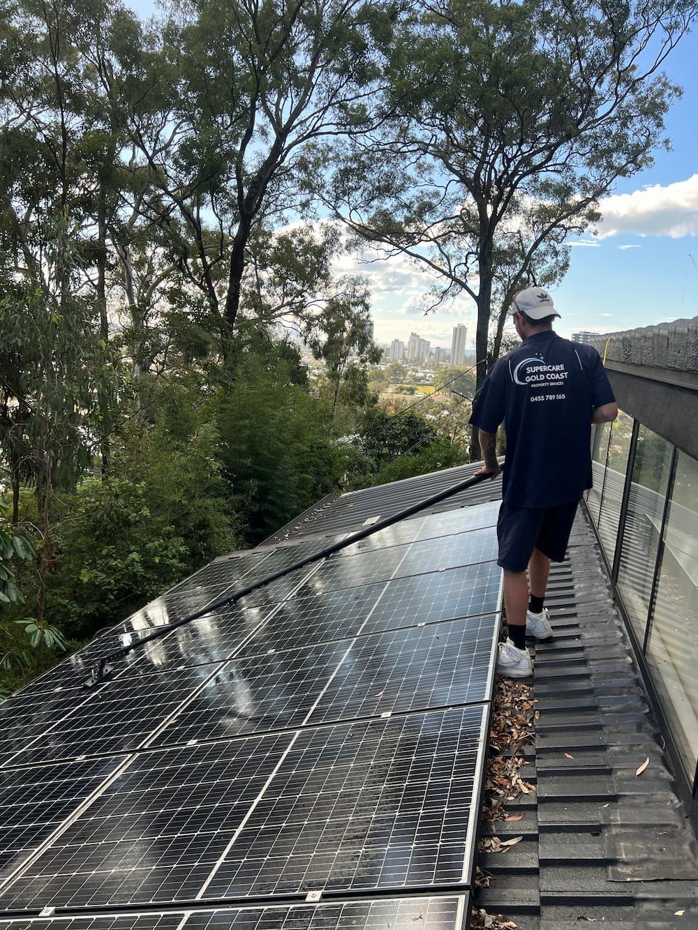 A Man Is Cleaning A Solar Panel With A Soft Pressure Washer — Supercare Gold Coast in Miami, QLD