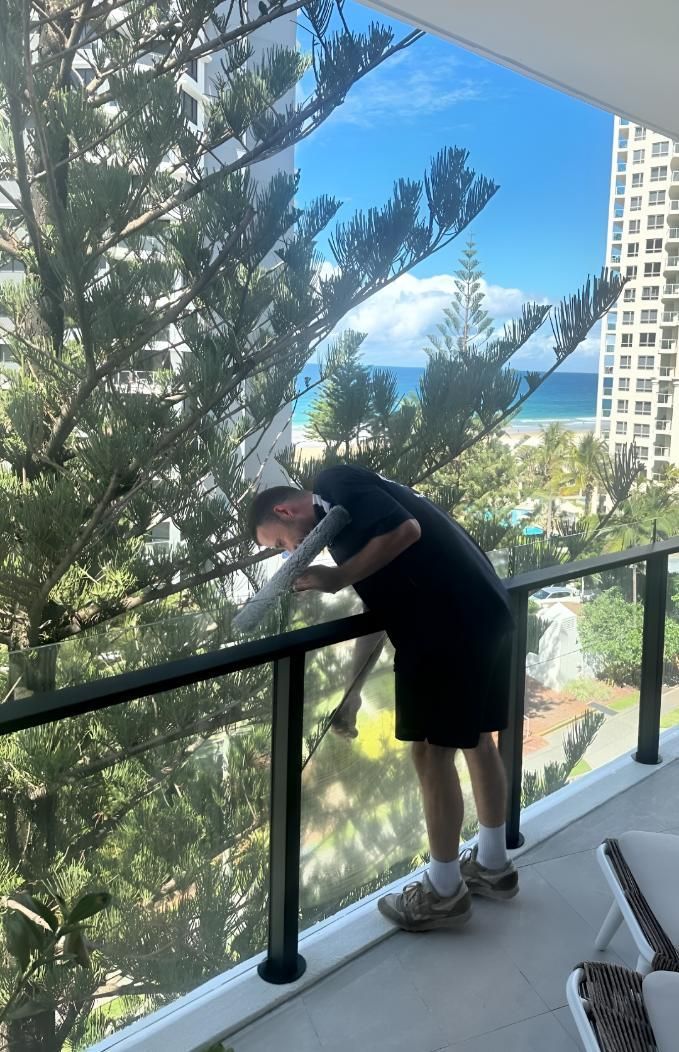 Man is Standing on a Balcony Cleaning a Window — Supercare Gold Coast in Miami, QLD