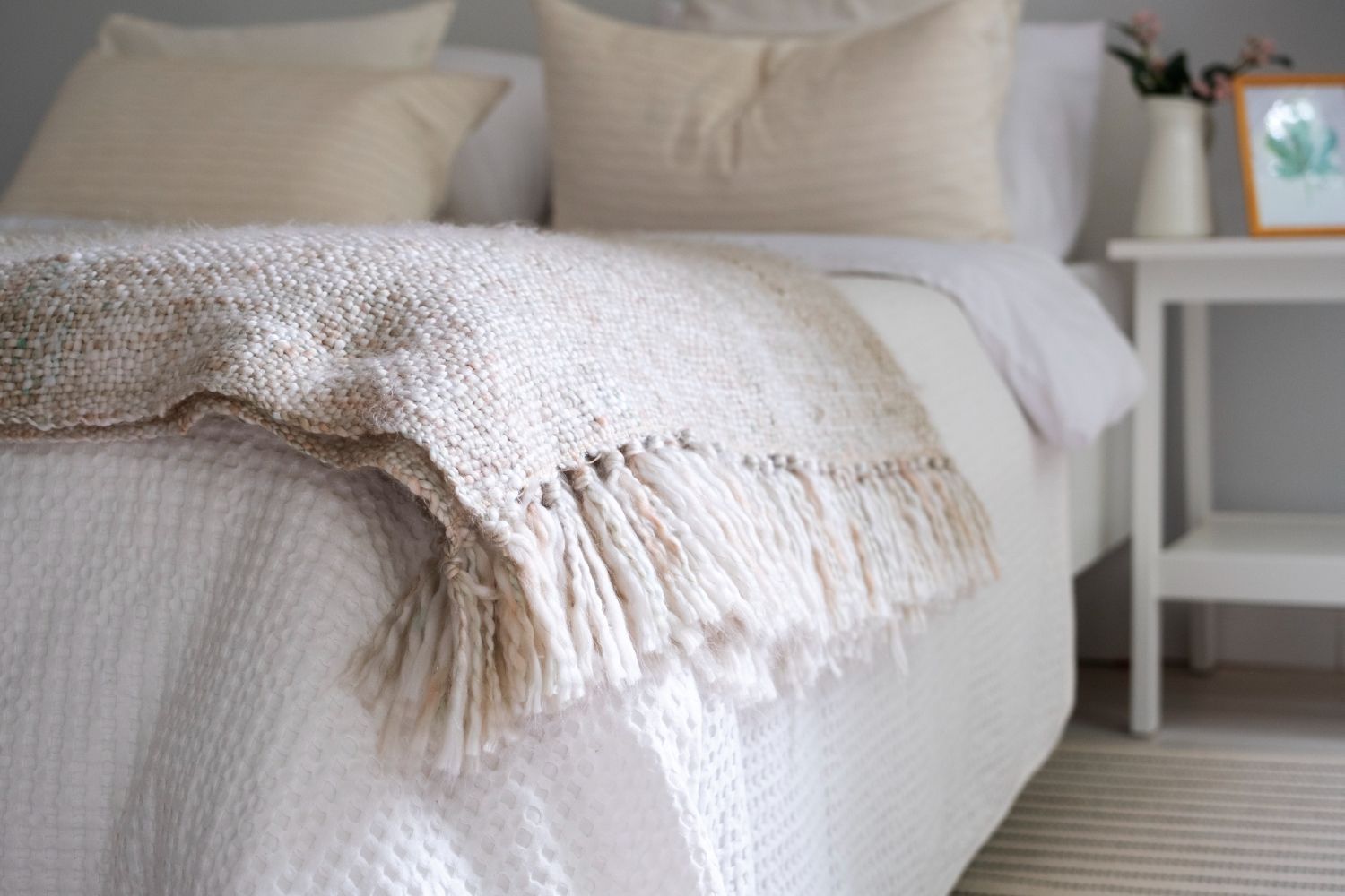 Cama acogedora con sábanas blancas y una manta de punto color crema en un dormitorio luminoso.