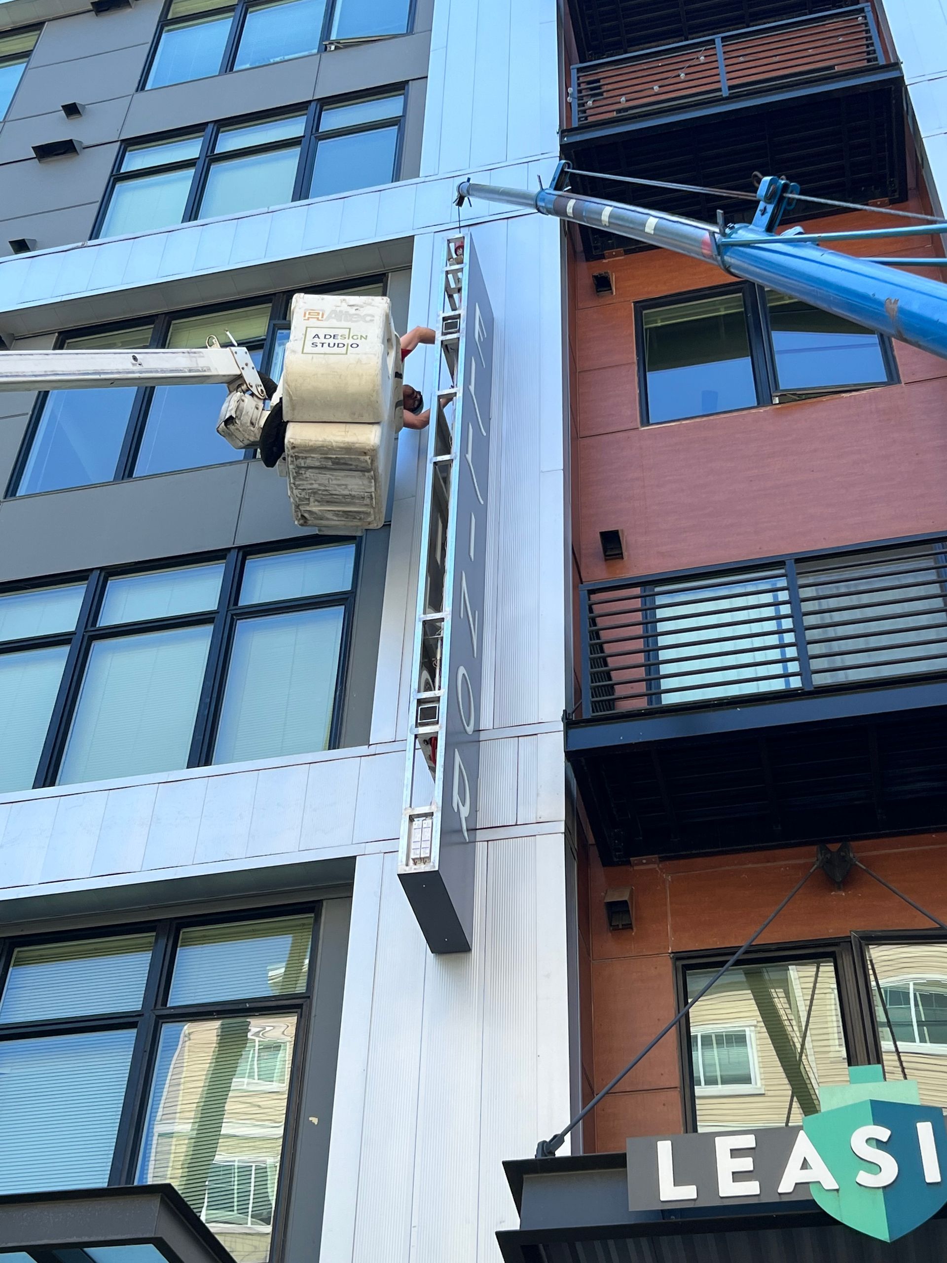 A person on a lift installs a vertical sign on a building