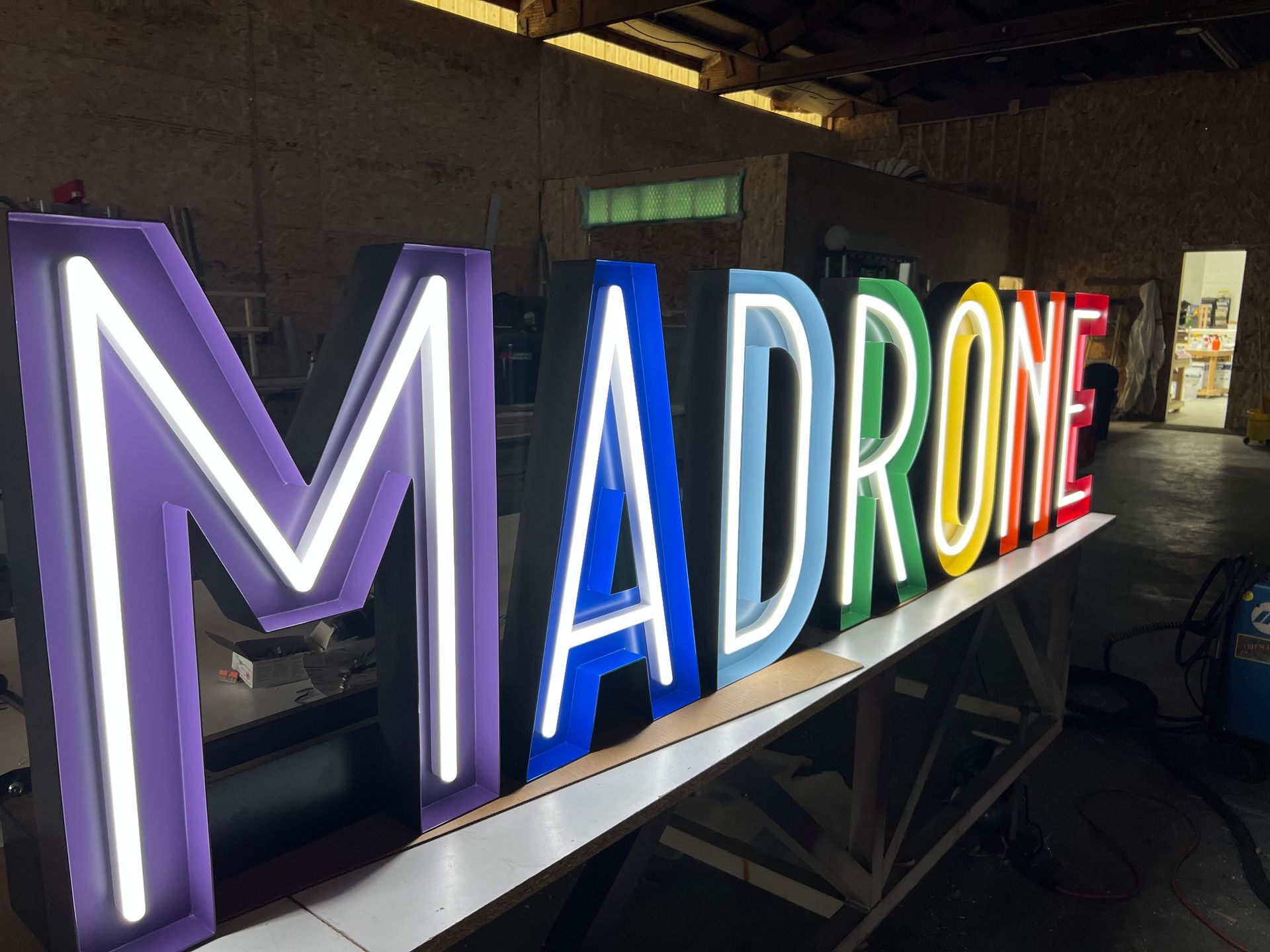 Neon sign in rainbow colors, lit against a workshop backdrop
