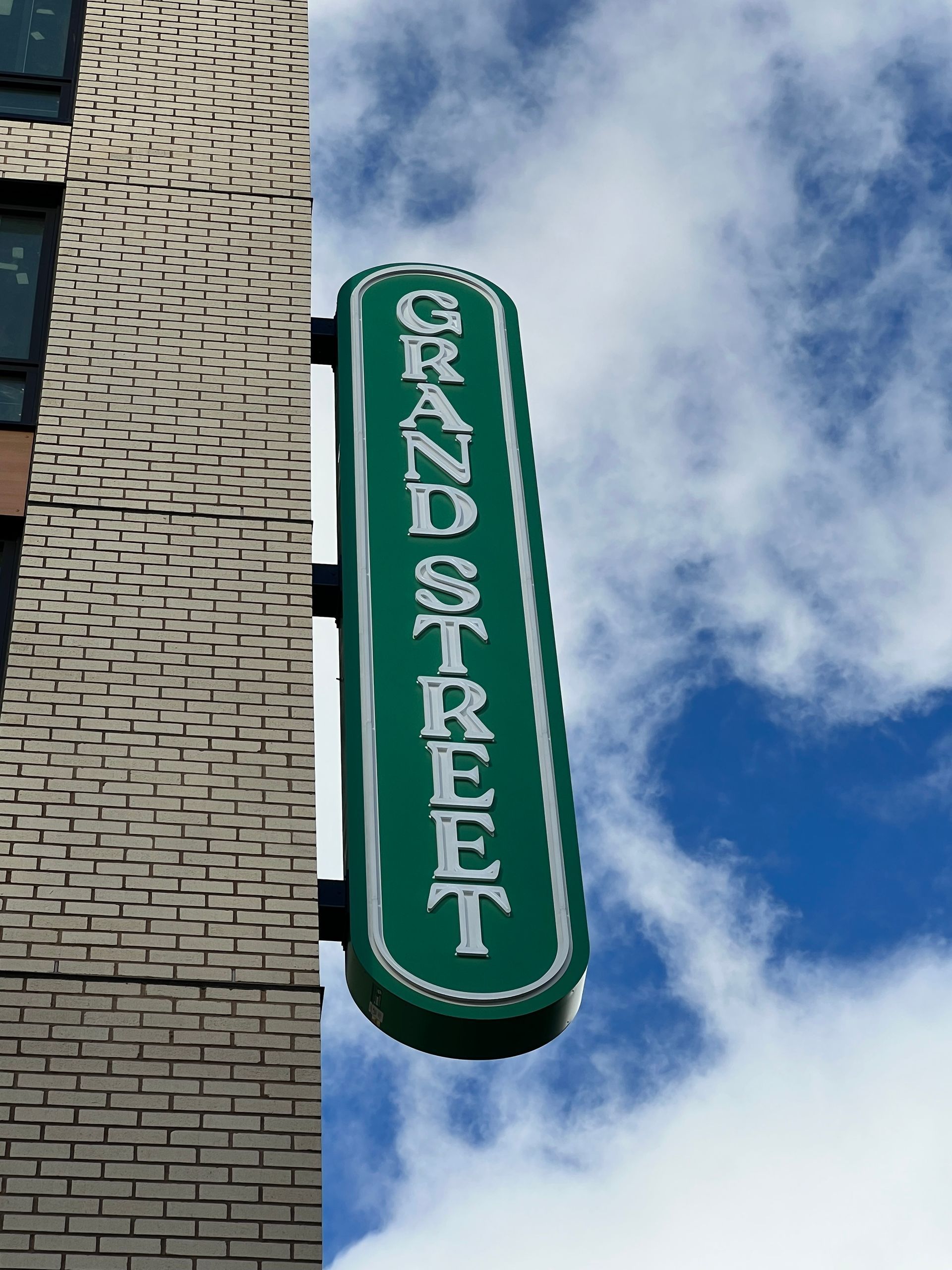 Green sign against a blue sky with clouds, mounted on a brick building