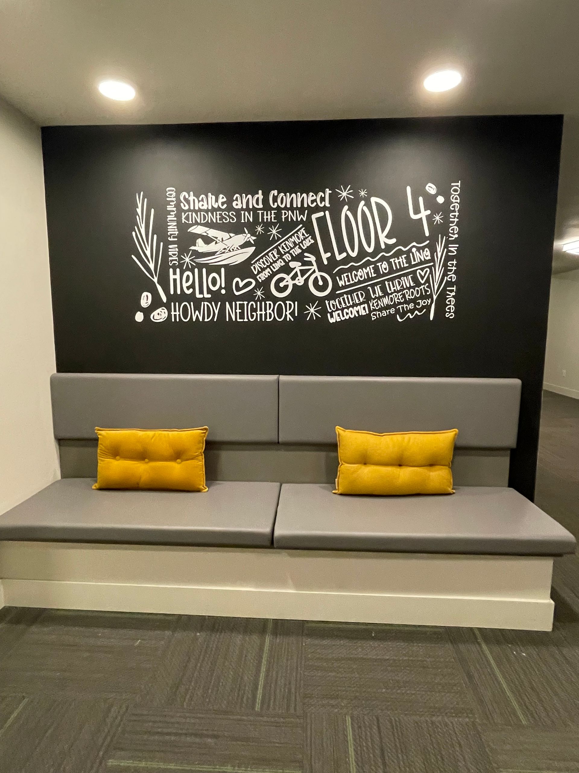 Built-in bench with yellow pillows under a black wall with white text and accents