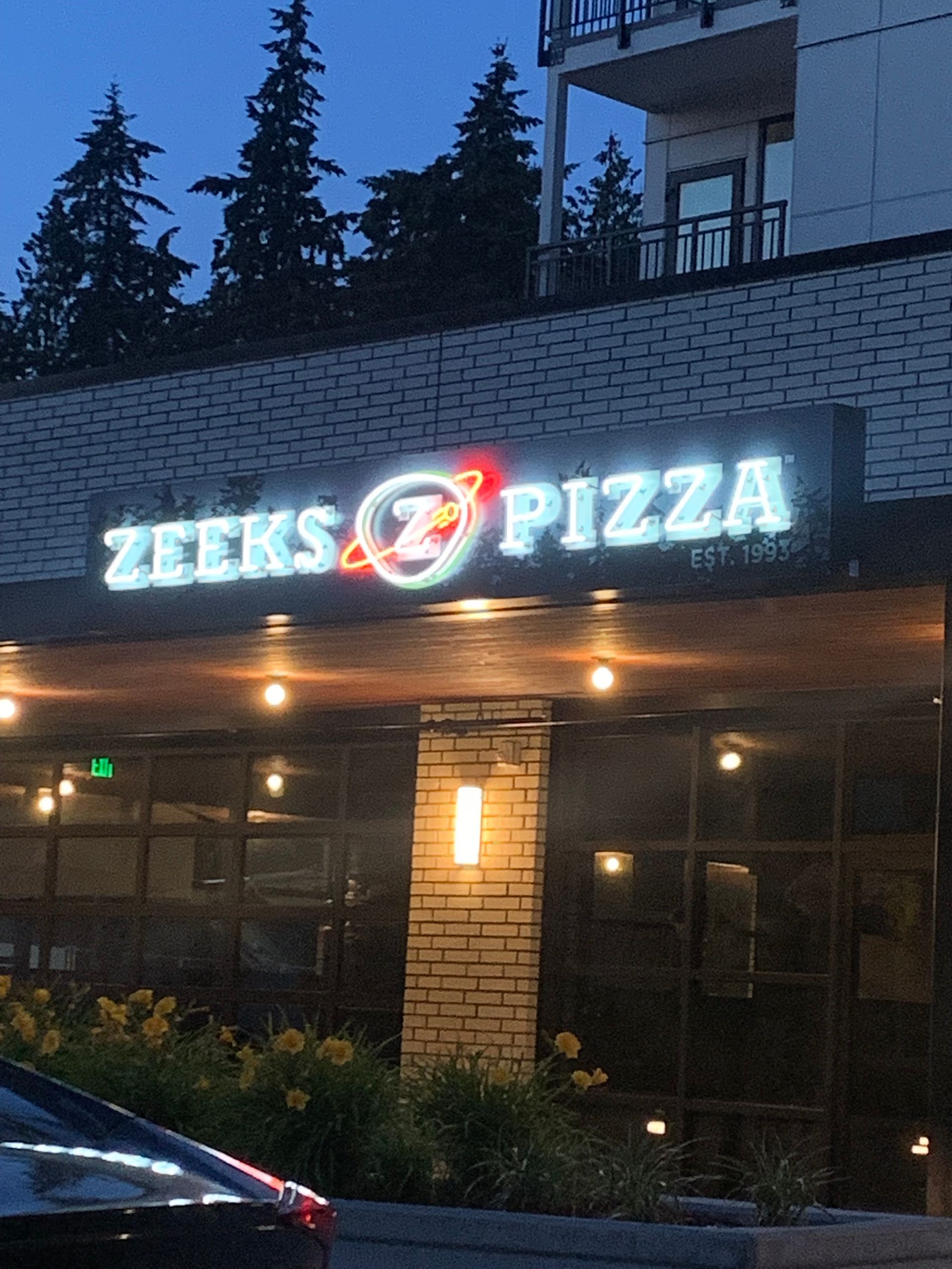 Zeeks pizza neon sign on building facade at dusk